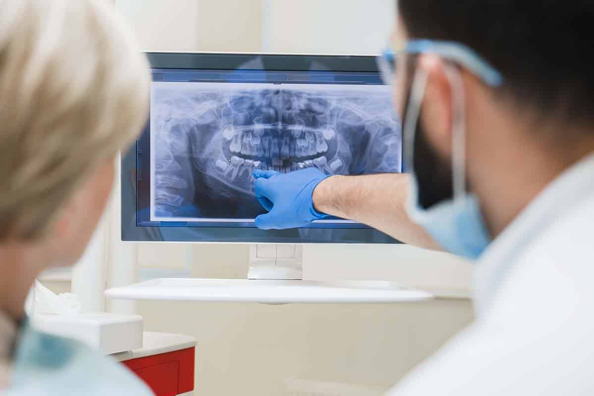 Dentist showing explaining an x-ray photo of jaws on computer screen to a female patient Bone Degeneration in Jaw - How to Prevent Bone Loss - Pristine ...